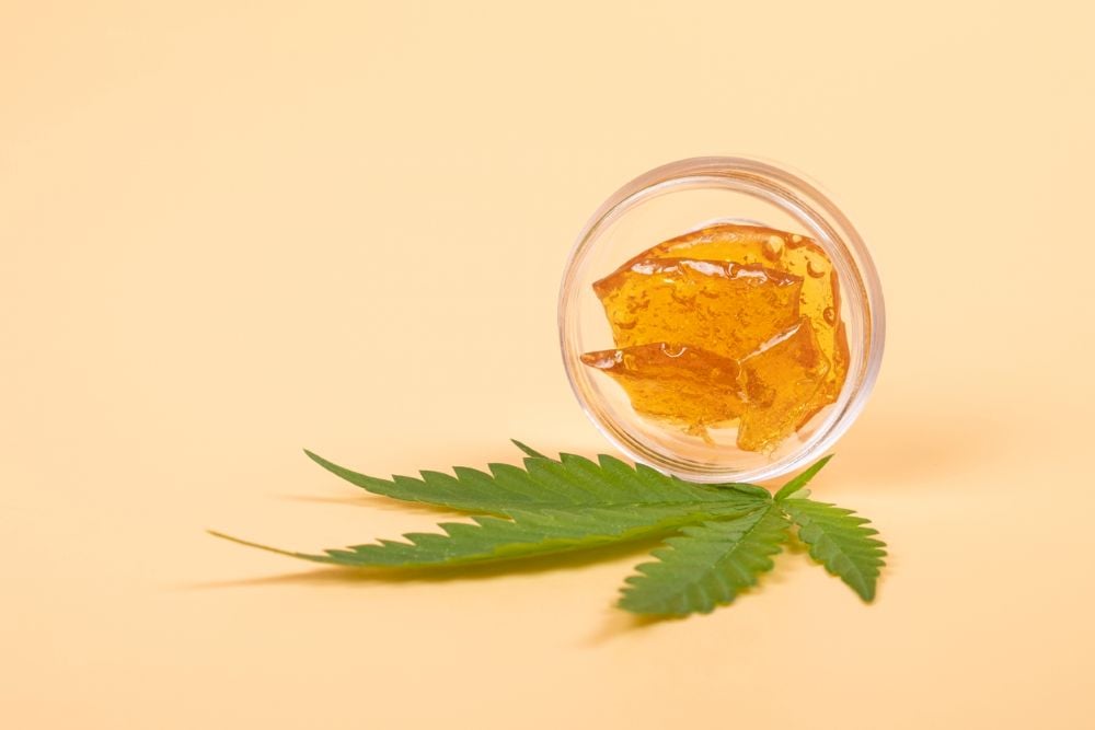Rosin: sheets of translucent amber resin in a jar next to a cannabis leaf